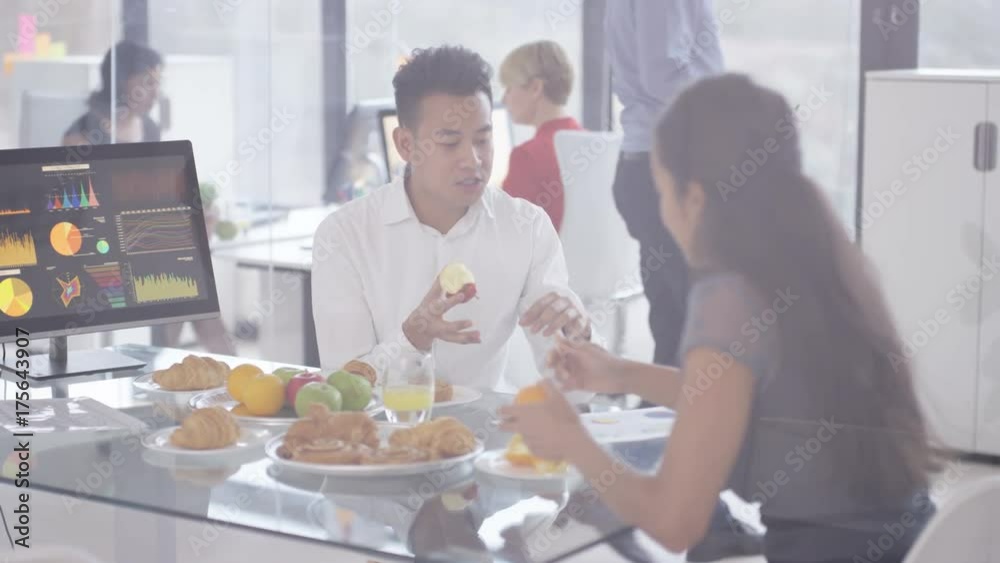 Business man & woman having a meeting, desk laid out with fruit & pastries Business man & woman having a meeting, desk laid out with fruit & pastries