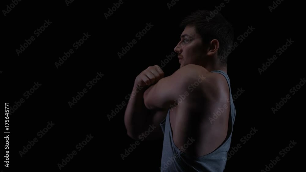 Fit young man with muscular physique stretching against black background Fit young man with muscular physique stretching against black background