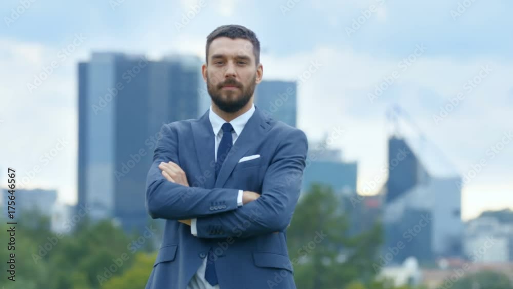 Successful Business Man Crosses Arms and Smiles in the Background Skyscrapers and Business Centre of the Big City is Visible. Shot on RED EPIC-W 8K Helium Cinema Camera. Successful Business Man Crosses Arms and Smiles in the Background Skyscrapers and Business Centre of the Big City is Visible. Shot on RED EPIC-W 8K Helium Cinema Camera.