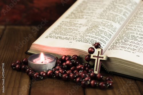 Fotografia Bible crucifix and beads with a candle on a brown wooden table