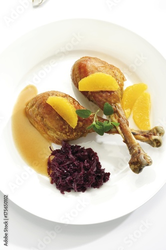 Roast chicken legs or drumsticks garnished with two orange segments, red cabbage, green leaves and gravy