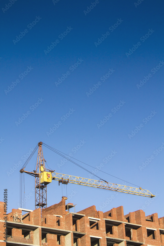 A yellow crane builds a residential building of red brick
