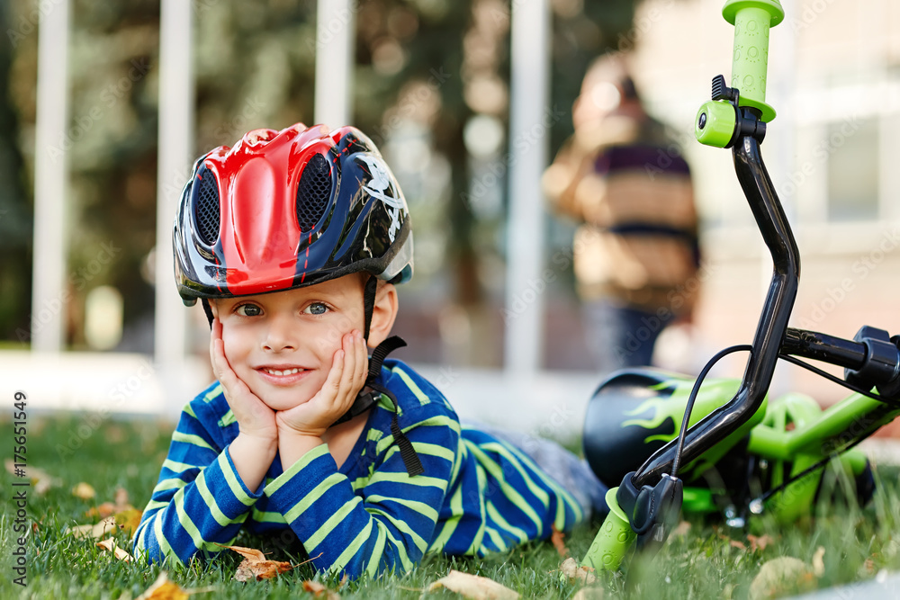 Boy in helmet sitting on grass with blue balance bike run bike. Healthy preschool children summer activity. Boy in helmet sitting on grass with blue balance bike run bike. Healthy preschool children summer activity.