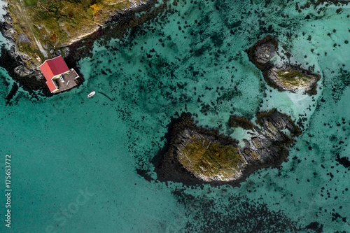 Aerial shot of small islands surrounded by limpid azure blue sea water. Red fishery house on the shore. Rebbenesoya, Norway