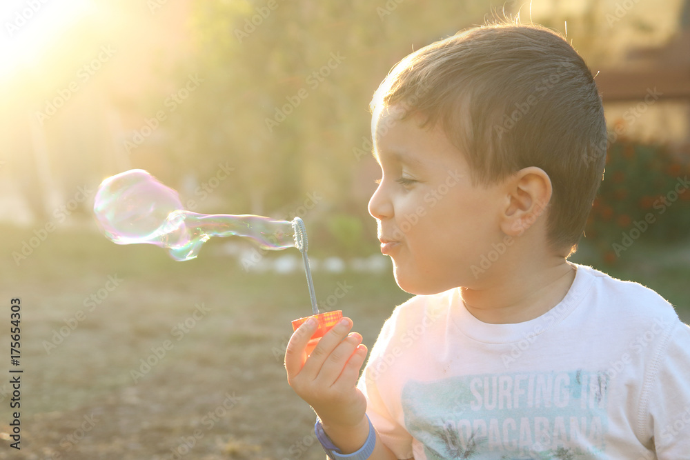 little child blowing soap bubbles in a field at sunset with golden sunlight