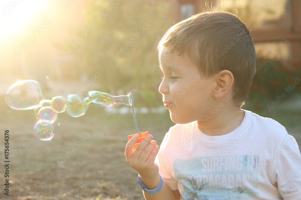 little child blowing soap bubbles in a field at sunset with golden sunlight little child blowing soap bubbles in a field at sunset with golden sunlight