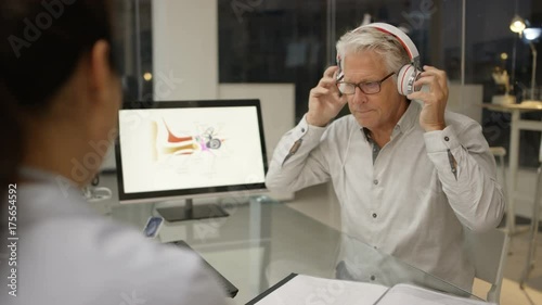  Mature man wearing headphones, getting a hearing test with audiology doctor.  photo