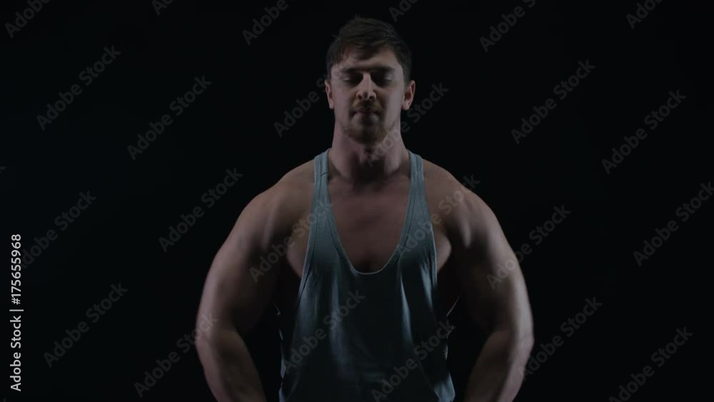 Fit young man with muscular physique lifting weights against black background Fit young man with muscular physique lifting weights against black background