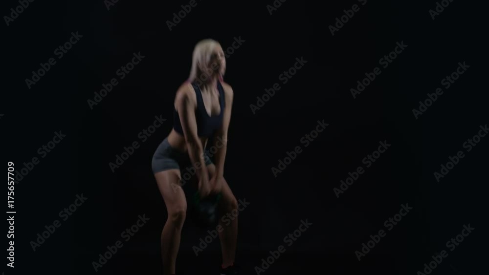 Fit young woman working out with kettle bell weight against black background Fit young woman working out with kettle bell weight against black background
