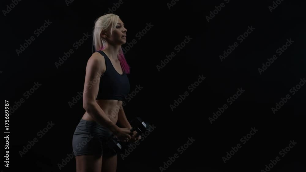 Fit woman with athletic physique lifting weights against black background Fit woman with athletic physique lifting weights against black background