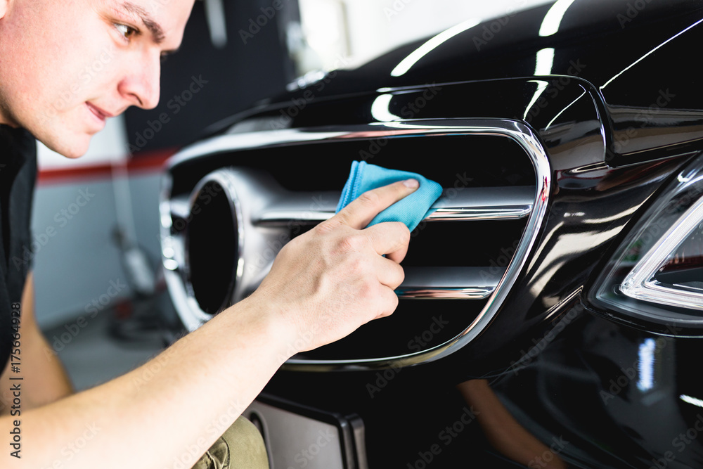 Naklejka premium A man cleaning car with microfiber cloth, car detailing (or valeting) concept. Selective focus. 