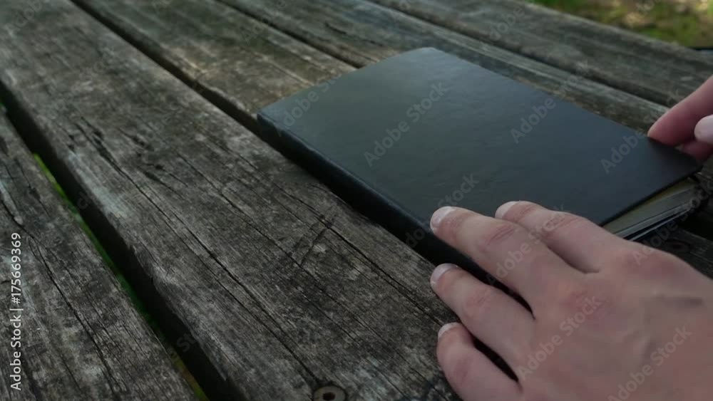 Open black moleskine with striped pages on wooden table in a outdoor park Open black moleskine with striped pages on wooden table in a outdoor park