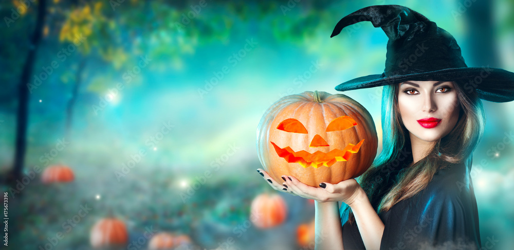 Halloween witch with a carved pumpkin and magic lights in a dark forest