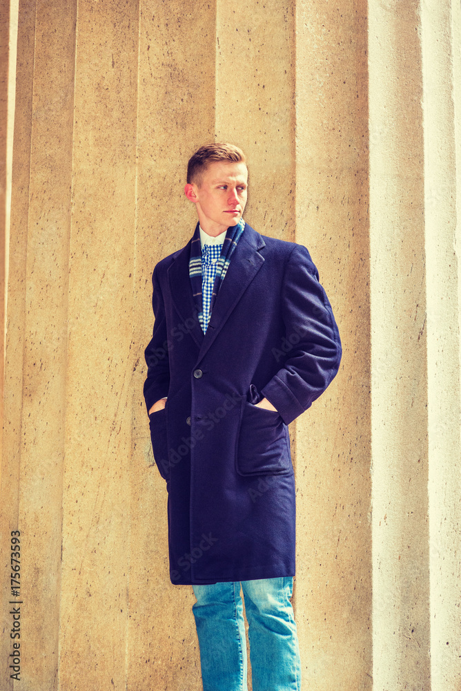 American teenage college student with blonde hair, wearing blue long woolen overcoat, scarf, jeans, hands in pockets, standing by column on campus in New York in winter, looking away. Filtered effect American teenage college student with blonde hair, wearing blue long woolen overcoat, scarf, jeans, hands in pockets, standing by column on campus in New York in winter, looking away. Filtered effect