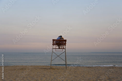 Loving couple sits in a lifeguards chair at sunset