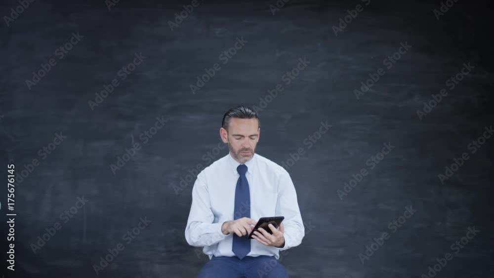 Man working on computer tablet & looking for inspiration on blank chalkboard Man working on computer tablet & looking for inspiration on blank chalkboard