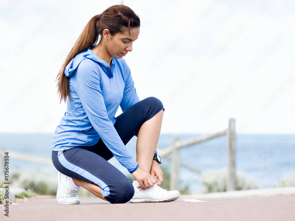 Woman runner tying shoelace at the seaside Woman runner tying shoelace at the seaside