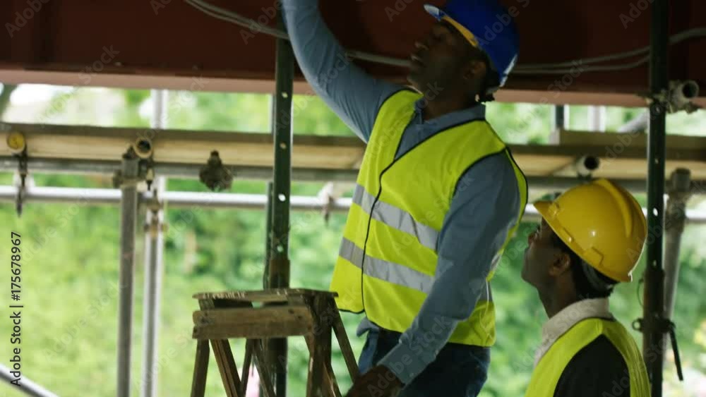 Builders working at construction site with female architect looking at plans Builders working at construction site with female architect looking at plans