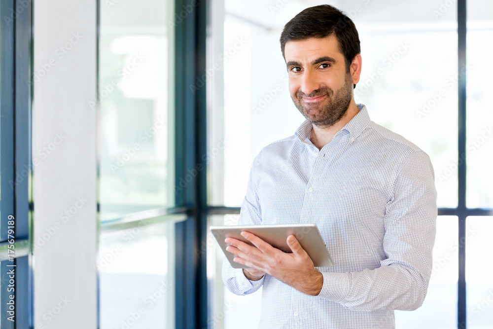 Young handsome businessman using his touchpad standing in office Young handsome businessman using his touchpad standing in office