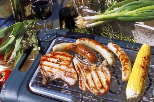 Outdoor barbecue, meat chops, sausages, spring onions, herbs, corn on the cob, red wine photo