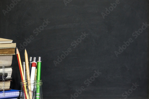 Chalkboard with pecil, pen, books on wooden table. Education concept.