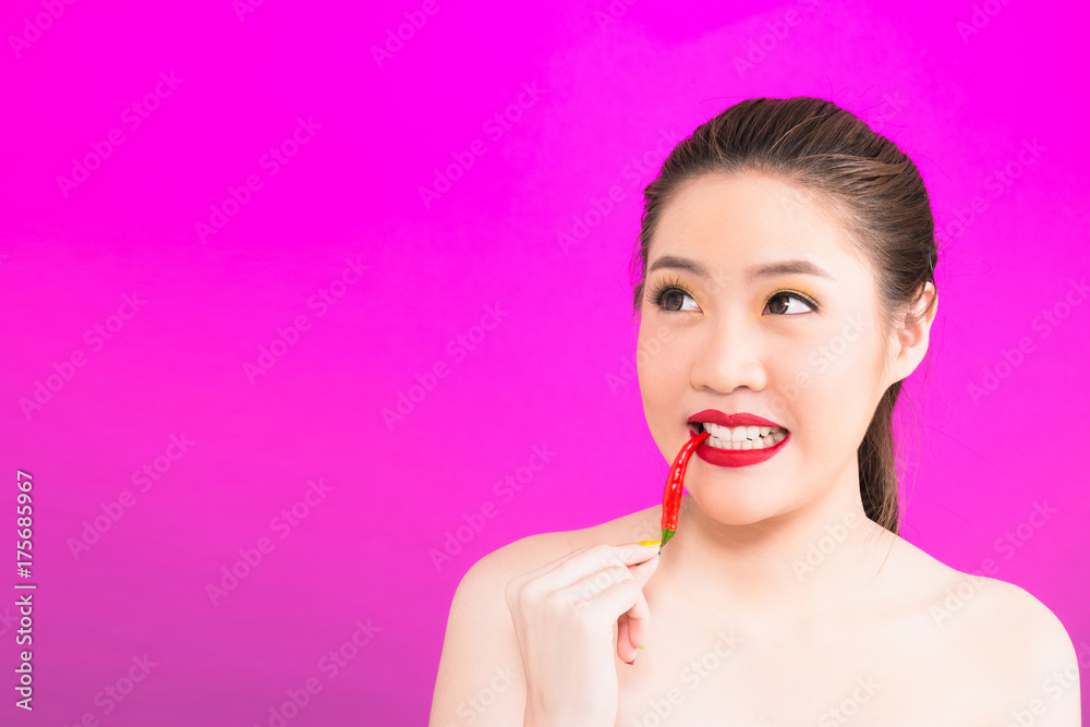 Young Asian woman biting chili isolated in pink background. Young Asian woman biting chili isolated in pink background.