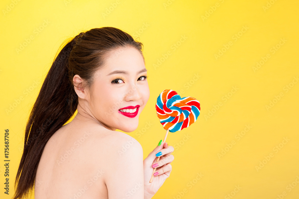 Young Asian woman holding lollipop isolated on yellow background.