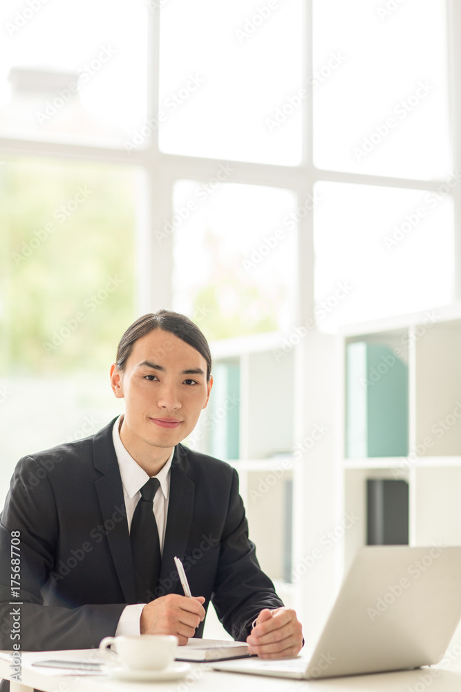 Young financial expert sitting by workplace with laptop in front Young financial expert sitting by workplace with laptop in front