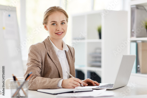 Foto Pretty young accountant sitting by desk, planning work and browsing in the net