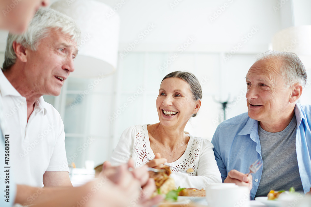 Cheerful senior friends gathered together at cozy small cafe and remembering funny stories from their past, they eating pastry and drinking fragrant coffee