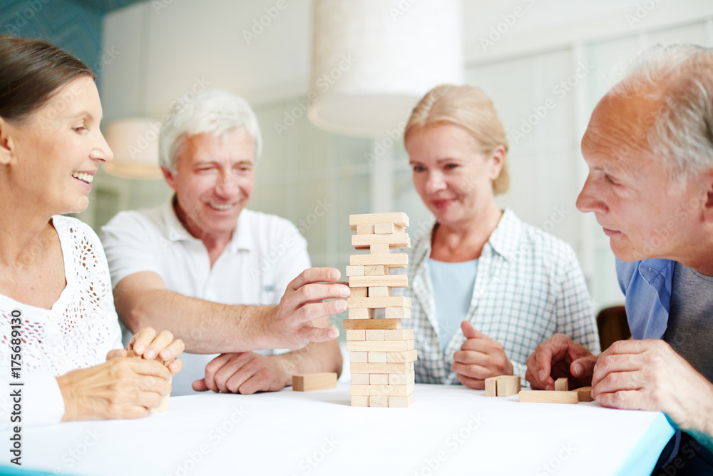 Long-awaited gathering of childhood friends: senior men and women with wide smiles having fun while sitting at cozy cafe and playing board game Long-awaited gathering of childhood friends: senior men and women with wide smiles having fun while sitting at cozy cafe and playing board game