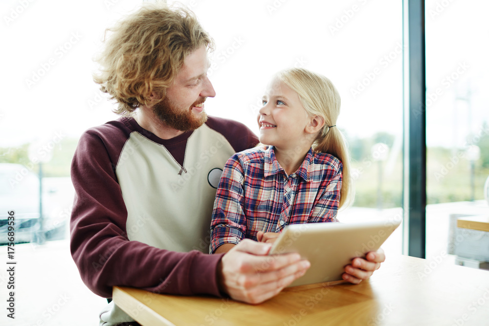 Contemporary child and her father with tablet spending leisure by watching curious video or movie and discussing it Contemporary child and her father with tablet spending leisure by watching curious video or movie and discussing it