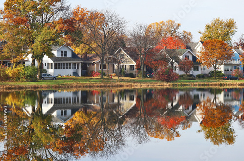 Autumn in a city background. Fall cityscape with private houses neighborhood along a pond. Colorful trees and houses reflected in a water. Midwest USA, Wisconsin. Classic american middle class homes.