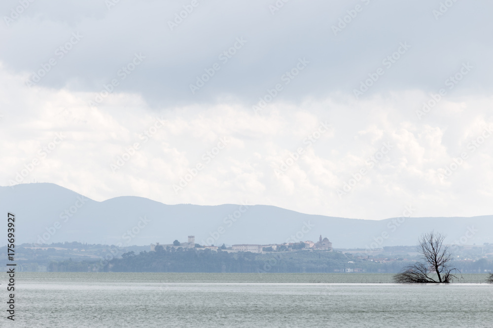 View of Castiglione del Lago town (Umbria, Italy), with Trasimeno lake and trees in the foreground