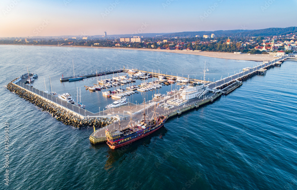 Sopot resort in Poland. Wooden pier (molo) with marina, yachts, pirate tourist ship, beach and vacation infrastructure. Aerial view at sunrise