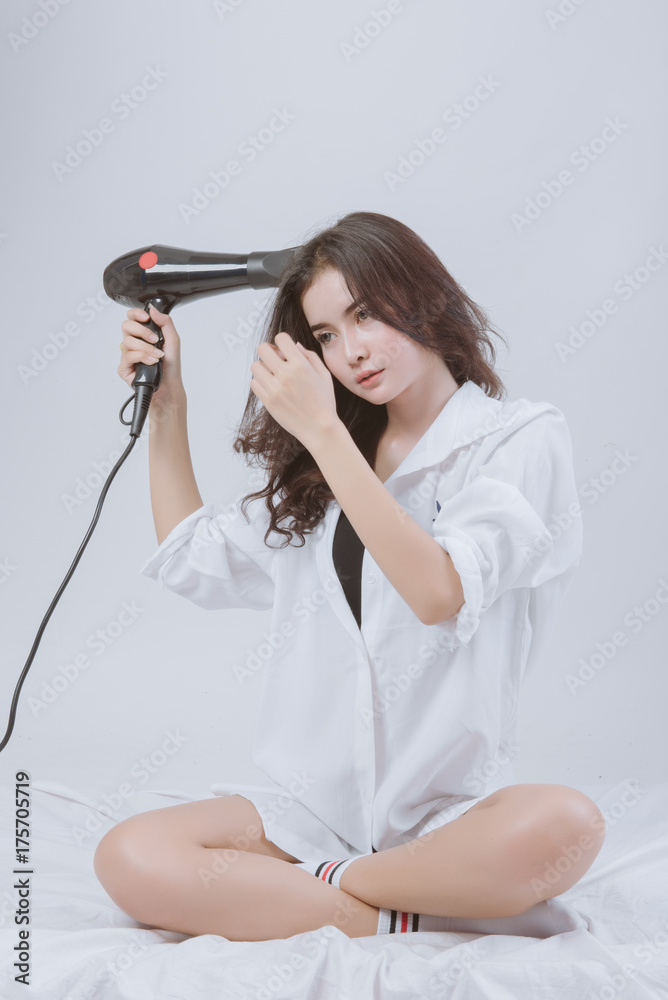 Young asian woman uses hair dryer on bed. Young asian woman uses hair dryer on bed.