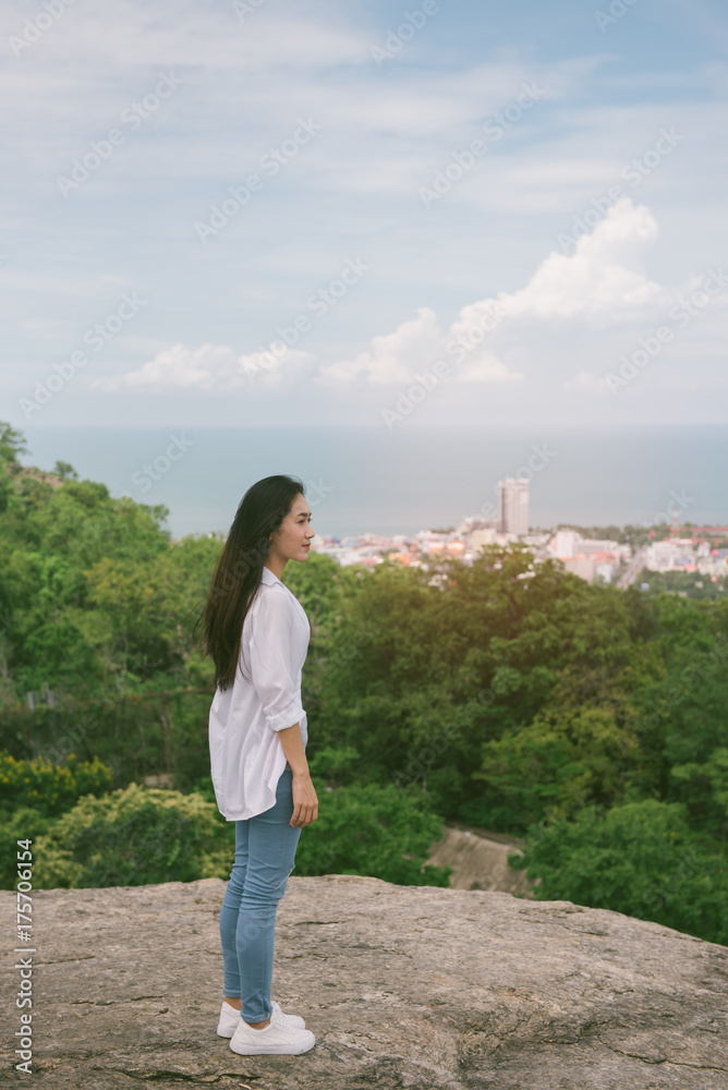 Young asian tourist  standing on top of a mountain and enjoying morning valley view. asian woman standing at cliff at Huahine beach in Thailand. vintage tone.