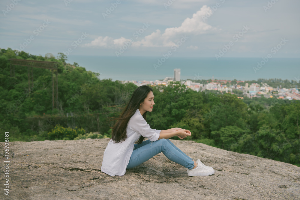 Young asian tourist  sit on top of a mountain and enjoying morning valley view. asian woman sit at cliff at Huahine beach in Thailand. vintage tone.