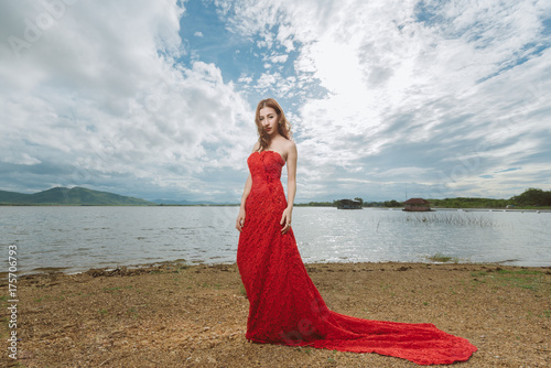 Asian beautiful girl in a long red dress standing over at lake view. Beautiful sexy fashion model woman posing, concept bride sexy.