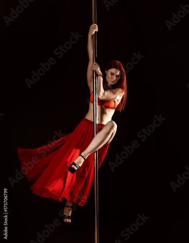 Young redhead athletic pole dance girl in a red dress on a black studio background photo