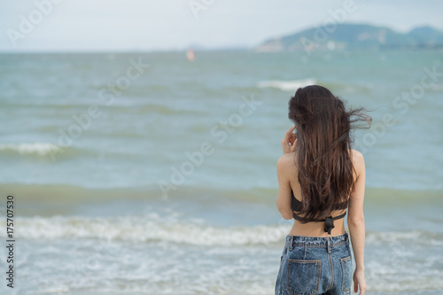 Back view image of young woman standing at beach and talking by her phone. Concept good signal.