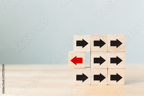 Fotografia Wooden block with red arrow facing the opposite direction black arrows, Unique, think different, individual and standing out from the crowd concept