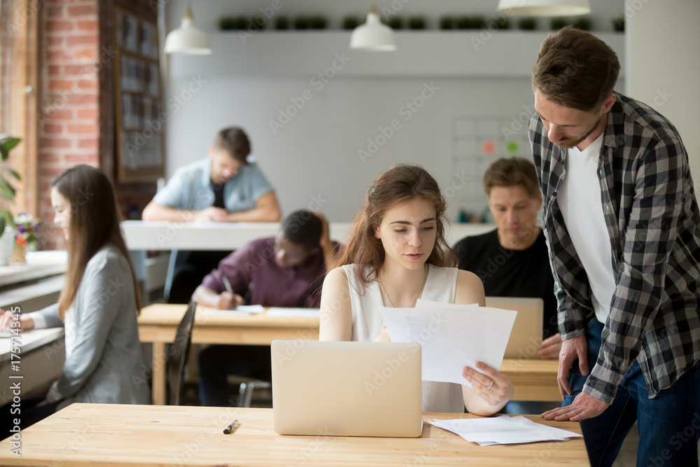Fototapeta premium Young female entrepreneur holds paperwork, explains information in documents to coworker. Job supervisor tells male employee specifics of workflow, approving business report, verifying work strategy.