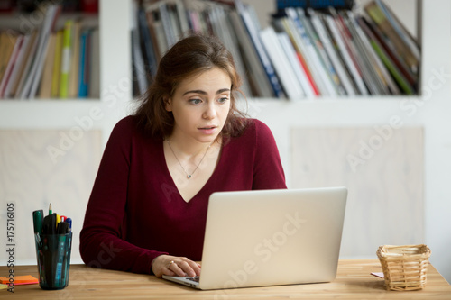 Young casual businesswoman staring at laptop screen with surprised expression. Female entrepreneur looking at computer with blank stare, received unexpected high bill, got email from unhappy customer.