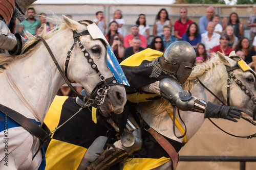 Two medieval warriors in armor, race in horses in the arena.