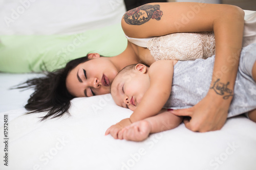 Beautiful mother and cute little baby boy sleeping together on bed.