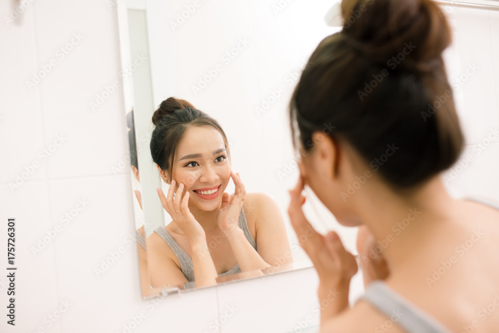 Smiling young woman looking to mirror at home bathroom Smiling young woman looking to mirror at home bathroom