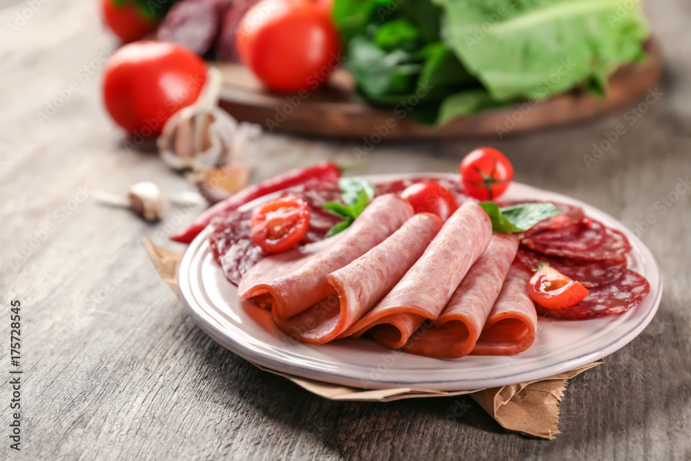 Plate with delicious sliced sausages on wooden table