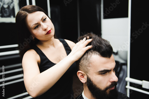 Master cuts hair and beard of men in the barbershop, hairdresser makes hairstyle for a young man