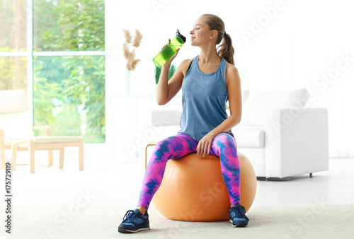 Young sporty woman drinking water at home